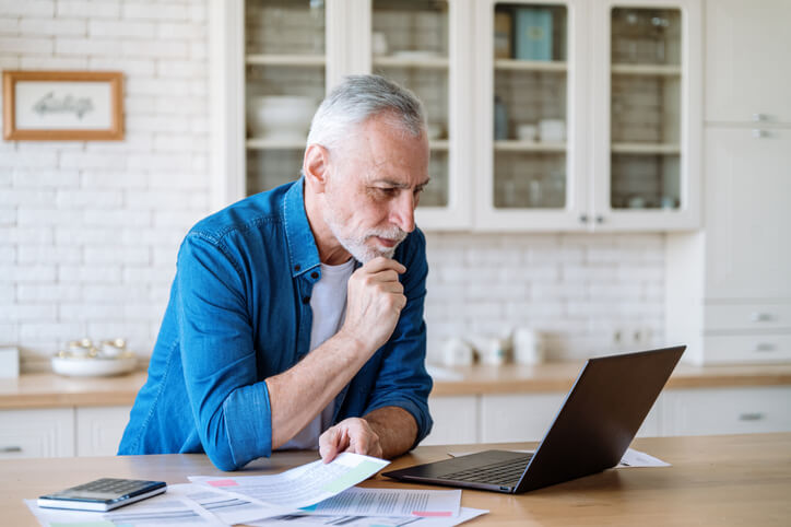 Focused mature man looking at laptop screen, calculate expenses, paying bills and taxes online. Busy male doing paperwork at home and managing retirement funds