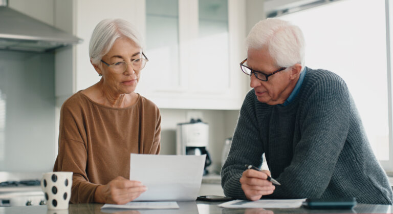 Senior couple, bills and budget in home for retirement savings, planning loan investment and financial administration. Old man, elderly woman and reading documents to review pension report in kitchen