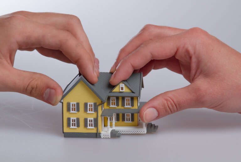 Human Hands Holding a Model of a House on Grey Background